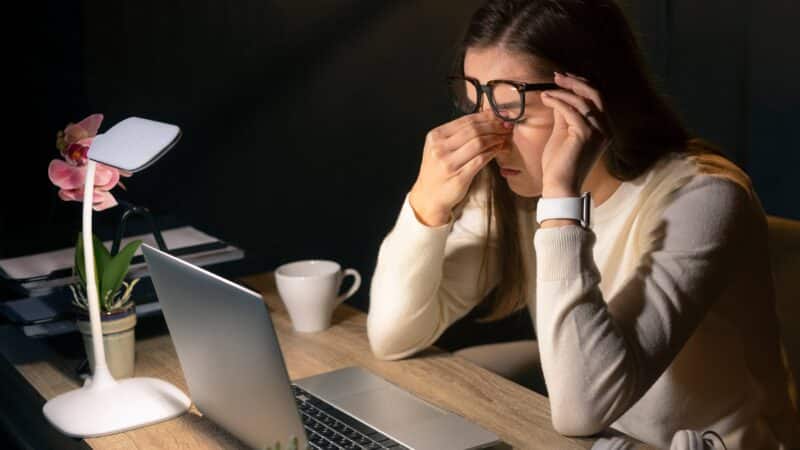 Profissional sentindo os efeitos da Síndrome da Visão de Computador após um longo dia de trabalho em frente à tela.